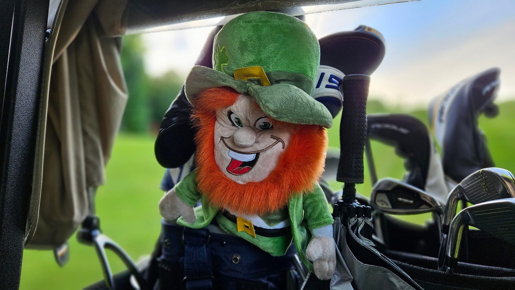 A stuffed leprechaun riding along in a golf bag
